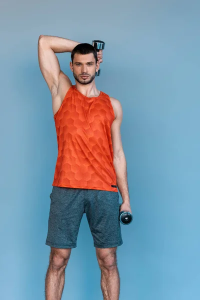 Handsome sportsman exercising with dumbbells on blue — Stock Photo