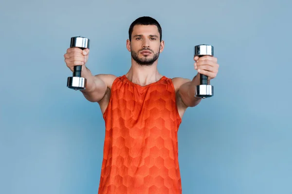 Guapo deportista haciendo ejercicio con mancuernas aisladas en azul - foto de stock