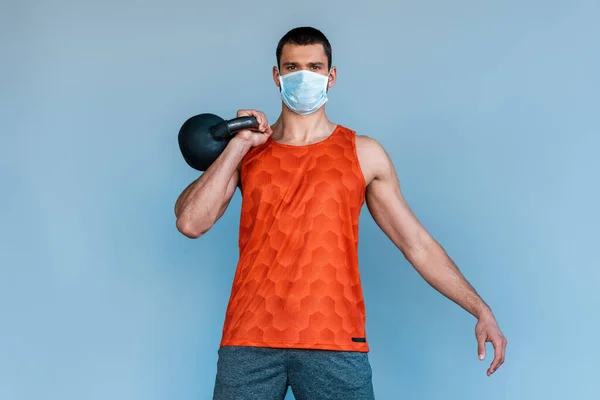 Sportsman in medical mask exercising with dumbbell isolated on blue — Stock Photo