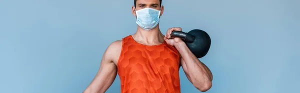 Panoramic shot of sportsman in medical mask exercising with dumbbell isolated on blue — Stock Photo