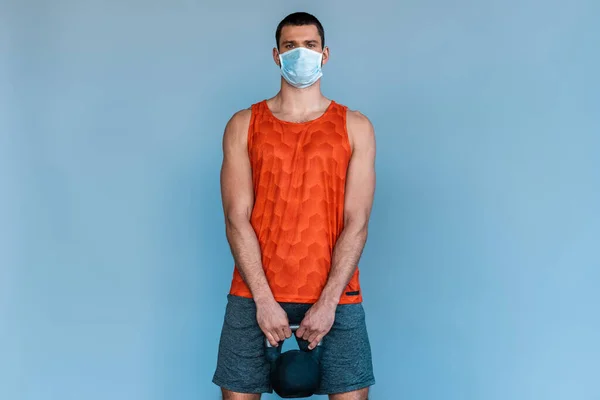 Deportista en máscara médica haciendo ejercicio con mancuerna aislada en azul - foto de stock