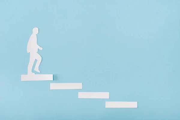 Vista superior del hombre de papel en la escalera de carrera sobre fondo azul - foto de stock