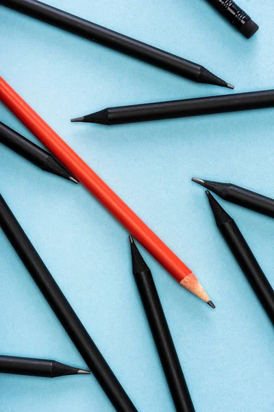 Vue du dessus du crayon rouge unique parmi le noir sur fond bleu — Photo de stock