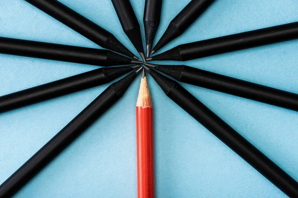 Top view of unique red pencil among black on blue — Stock Photo