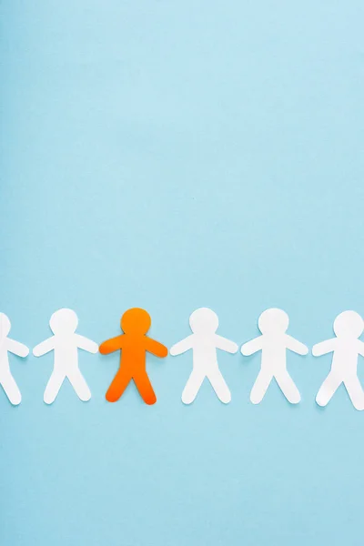 Top view of unique orange paper man among white on blue — Stock Photo