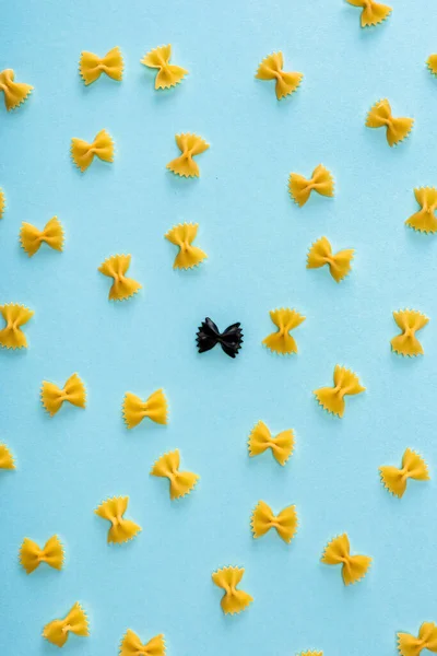 Pose plate avec des pâtes noires uniques parmi le jaune sur le bleu — Photo de stock