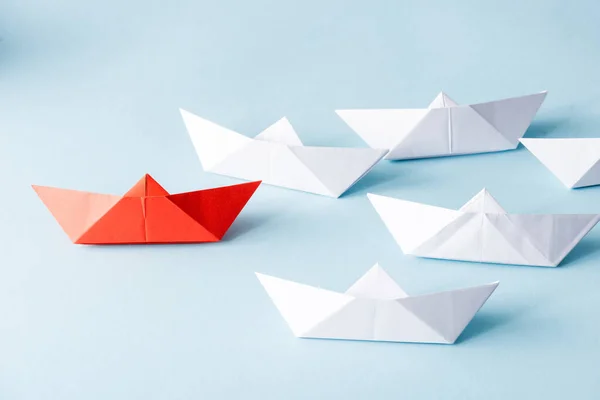 Unique red paper boat among white on blue background — Stock Photo