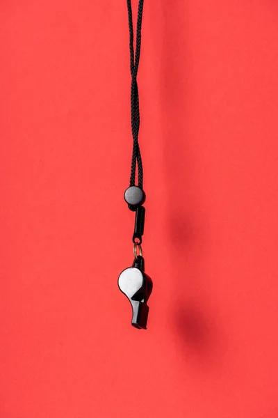 Black whistle on rope on red background — Stock Photo