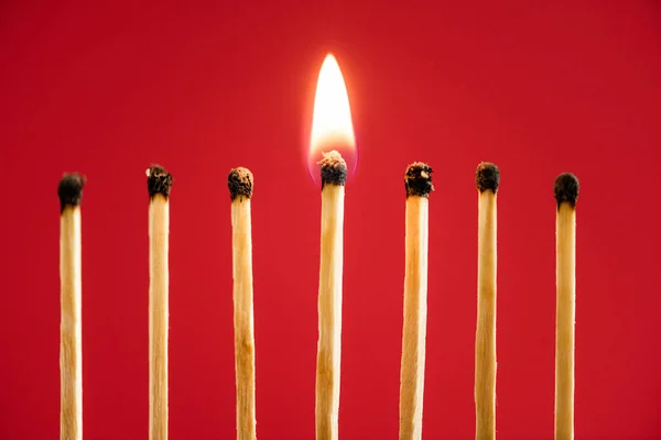 Match with fire among burned matches on red background — Stock Photo