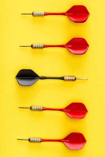 Flat lay with black dart among red on yellow background — Stock Photo