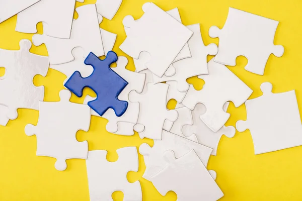 Top view of unique blue piece of puzzle among white on yellow — Stock Photo