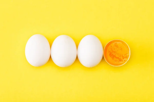 Vista superior do ovo cru metade entre ovos inteiros no fundo amarelo — Fotografia de Stock