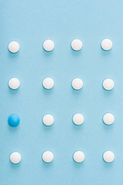 Flat lay with unique pill among white on blue background — Stock Photo