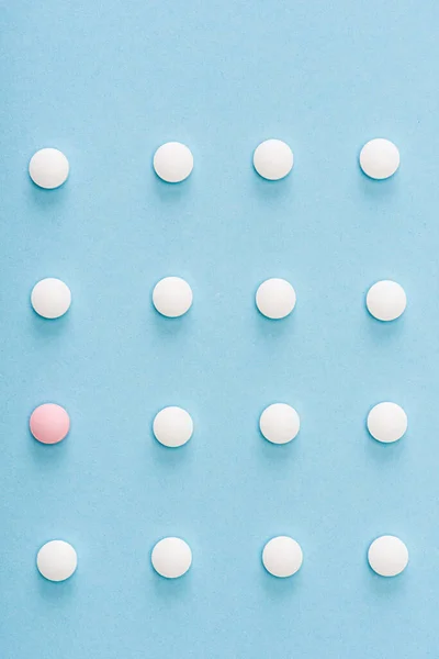Flat lay with pink pill among white on blue background — Stock Photo