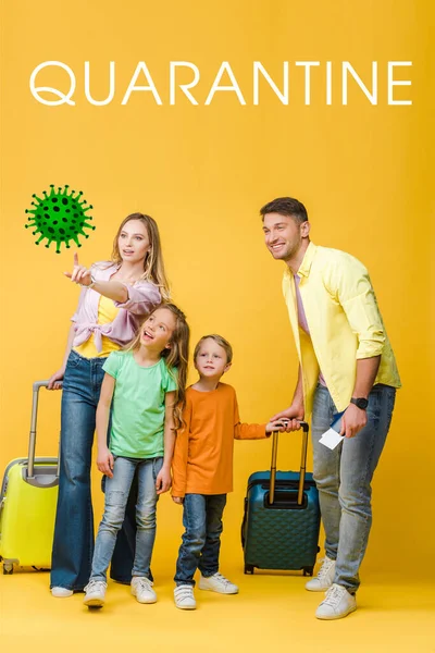 Família feliz de viajantes com bagagem, passaportes e bilhetes apontando para bactérias em amarelo, letras de quarentena — Fotografia de Stock