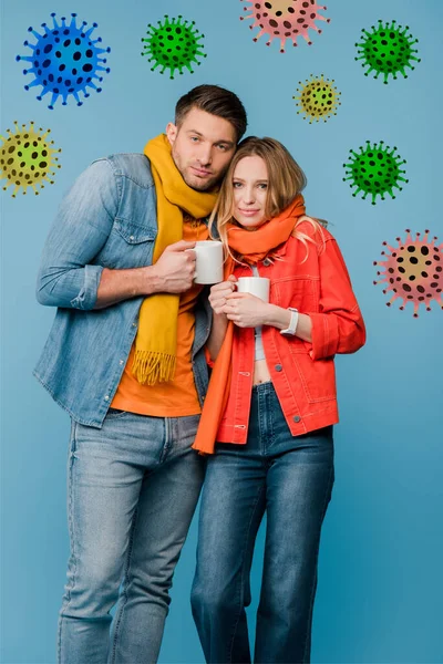 Pareja enferma en bufandas sosteniendo tazas con bebidas calientes aisladas en azul, ilustración de bacterias - foto de stock