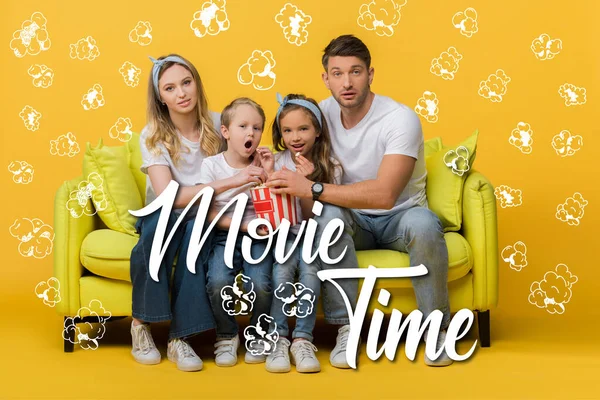 Familia sorprendida viendo la película en el sofá con palomitas de maíz cubo en amarillo, tiempo de la película y palomitas de maíz ilustración - foto de stock
