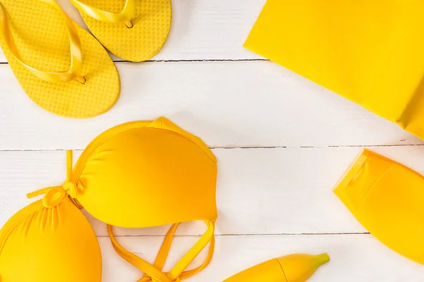 Vue du dessus des tongs jaunes près du maillot de bain et de la crème solaire sur une surface en bois blanc — Photo de stock