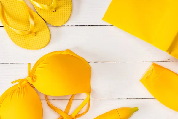 Top view of yellow flip flops near swimsuit and sunscreen on white wooden surface — Stock Photo