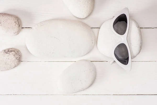 Вид зверху на морські камені з сонцезахисними окулярами на білій дерев'яній поверхні — стокове фото