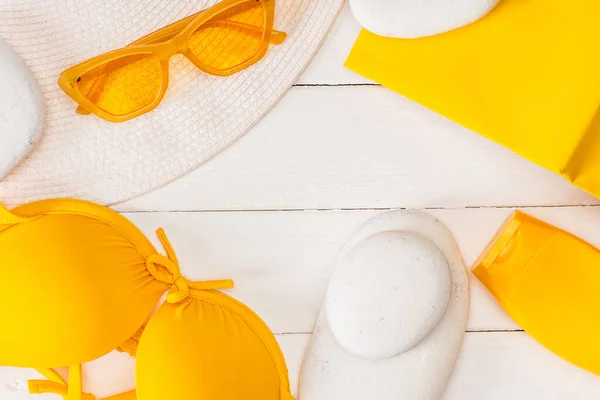 Vue du dessus du chapeau solaire, de la crème solaire avec livre jaune et des lunettes de soleil sur une surface en bois blanc — Photo de stock