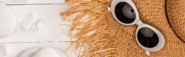 Panoramic shot of top view of straw hat with sunglasses and pebbles on white wooden surface — Stock Photo