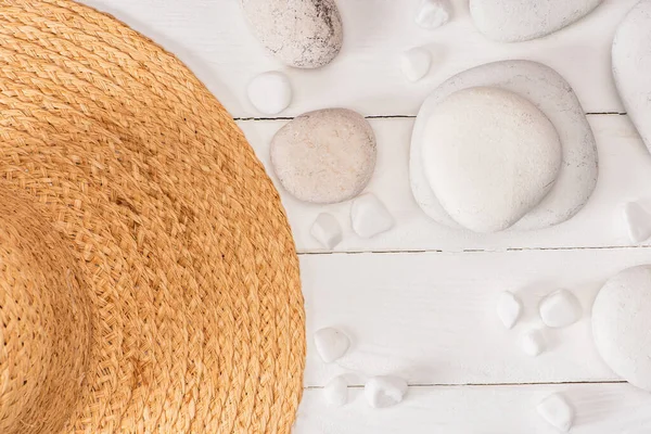 Vista dall'alto del cappello di paglia con pietre marine su sfondo di legno bianco — Foto stock