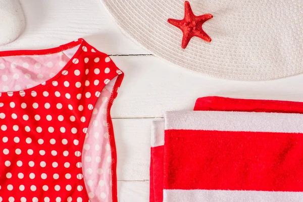 Vista superior del traje de baño cerca de la toalla rayada, sombrero de sol y estrella de mar roja en la superficie de madera blanca - foto de stock