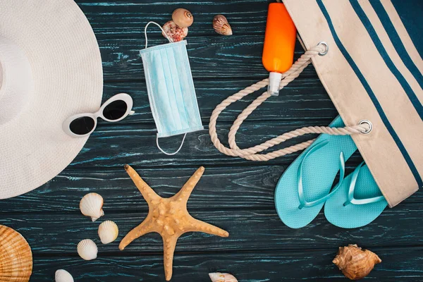 Vista dall'alto della maschera medica, infradito con cappello da sole e conchiglie sulla superficie di legno scuro — Foto stock