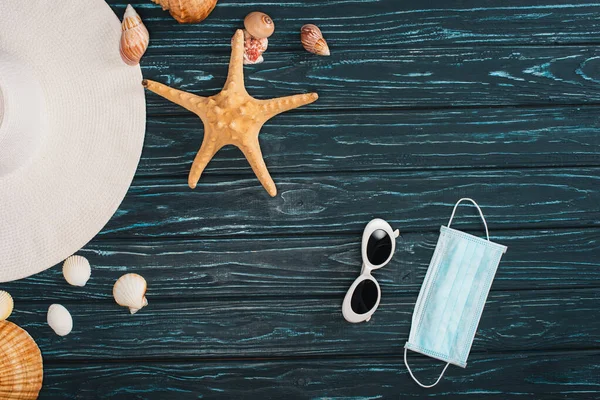 Top view of sun hat near medical mask, seashells and sunglasses on dark wooden surface — Stock Photo