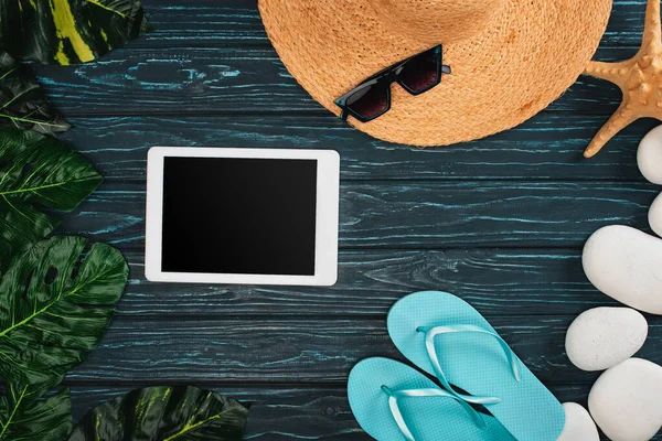 Vista superior do tablet digital perto de chapéu de palha, chinelos e folhas com pedras marinhas na superfície de madeira escura — Fotografia de Stock