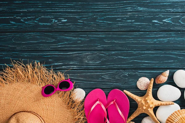 Vue de dessus du chapeau de paille près des lunettes de soleil roses, des tongs et des coquillages sur une surface en bois sombre — Stock Photo