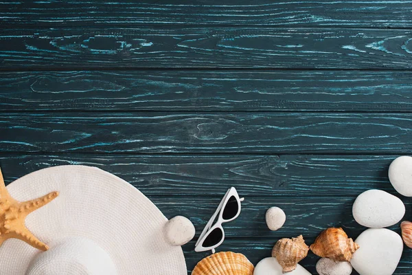 Top view of sun hat, sunglasses near sea stones and seashells on dark wooden background — Stock Photo