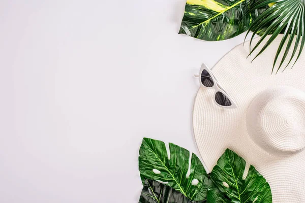 Top view of sunglasses and sun hat near green leaves of tropical plants on white background — Stock Photo