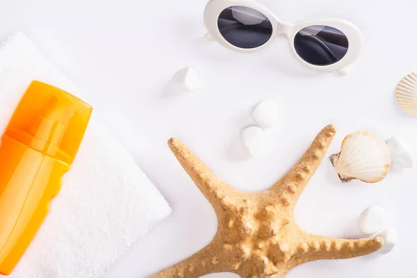 Вид зверху сонцезахисний крем на рушник біля зірок і сонцезахисних окулярів на білій поверхні — стокове фото