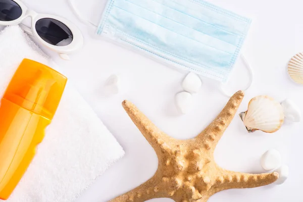 Muscheln von oben, Sonnencreme auf Handtuch und medizinische Maske auf weißem Hintergrund — Stockfoto