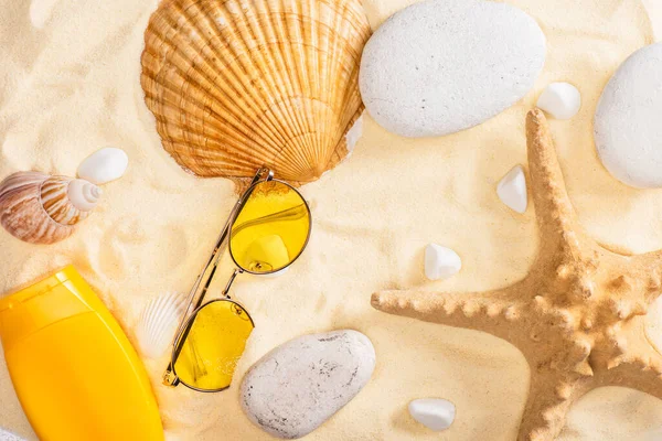 Верхній вигляд сонцезахисних кремів і сонцезахисних окулярів біля зірок і морських мушель на піску. — стокове фото