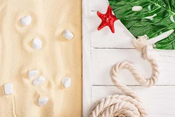 Top view of starfish, rope and green leaf on white wooden planks near pebbles on sand — Stock Photo