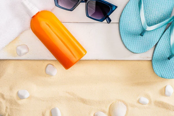 Top view of sunscreen, sunglasses and flip flops on white wooden planks near sea stones on sand — Stock Photo