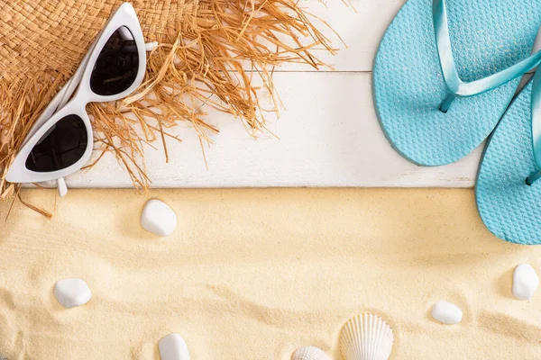 Draufsicht auf Strohhut neben Sonnenbrille und blauen Flip Flops auf weißen Holzplanken und Kieselsteinen im Sand — Stockfoto