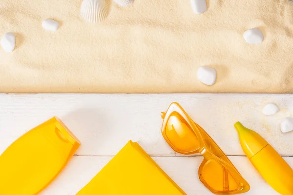 Top view of yellow sunglasses, book and sunscreens on white wooden planks near pebbles on sand — Stock Photo