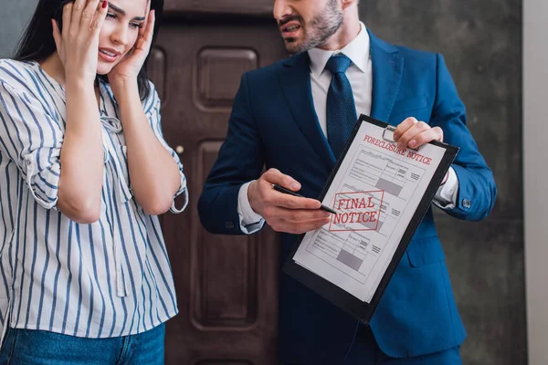Collector pointing at documents with foreclosure lettering near stressed woman in room — Stock Photo