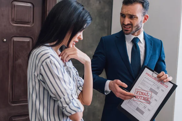 Irritated collector pointing at documents with foreclosure and final notice lettering near upset woman in room — Stock Photo