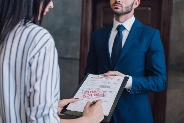 Cropped view of woman writing in documents with foreclosure and final notice lettering near collector in room — Stock Photo