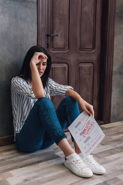 Worried woman holding document with foreclosure and final notice lettering and sitting near wall on floor in room — Stock Photo