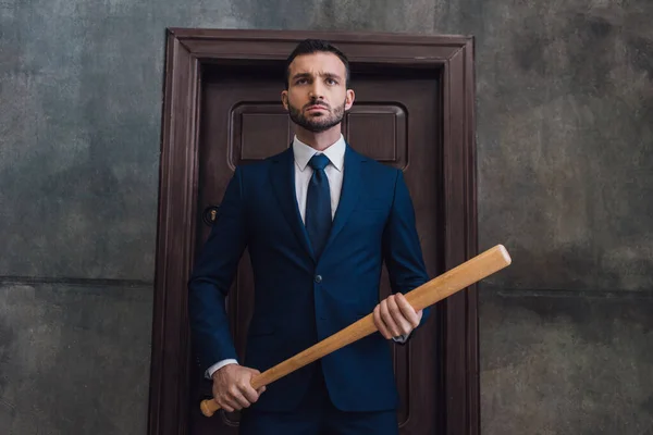 Coleccionista enojado sosteniendo bate de béisbol cerca de puerta en habitación - foto de stock