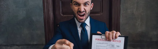 Panoramic orientation of angry collector with documents with foreclosure lettering pointing with finger and shouting in room — Stock Photo