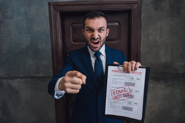 Angry collector with documents with foreclosure lettering pointing with finger and shouting in room — Stock Photo