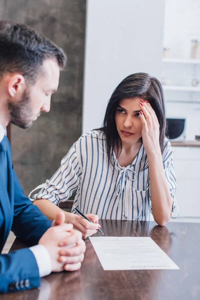 Selektiver Fokus der Frau, die den Stift in der Nähe des Dokuments hält und den Sammler mit geballten Händen am Tisch im Raum betrachtet — Stockfoto