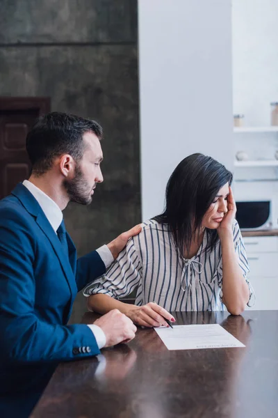 Sammler beruhigt verärgerte Frau mit Stift und Dokument am Tisch im Zimmer — Stockfoto